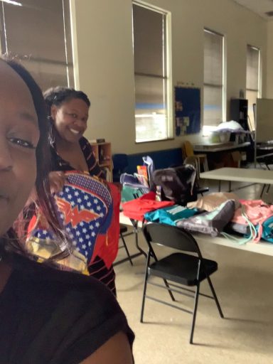 Backpack and Gym bag giveaway Two women smile while holding colorful artwork in a bright room with tables and chairs.
